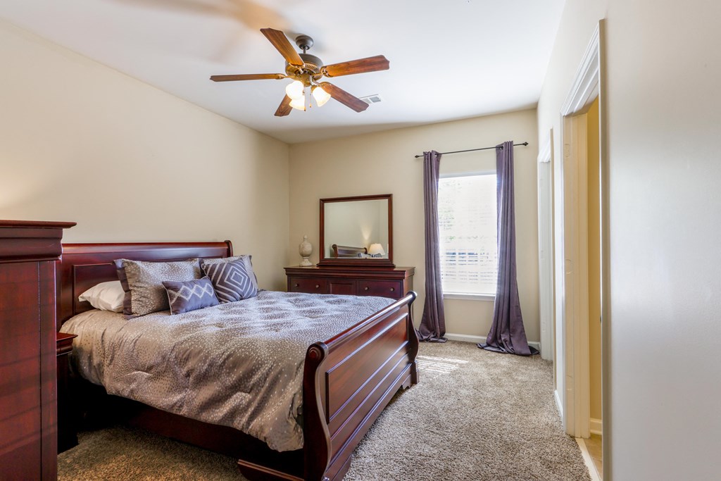 A bedroom with a bed, dresser, mirror, and window.