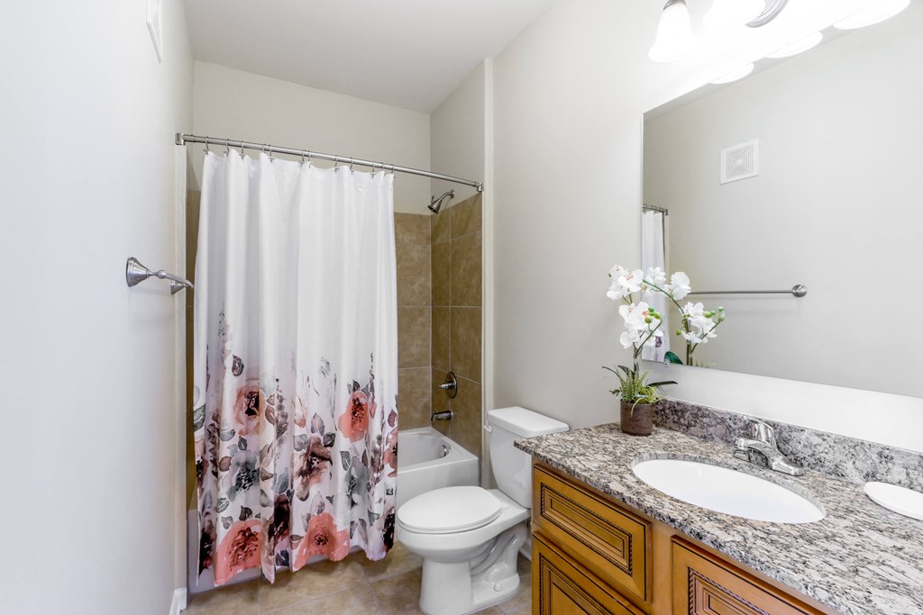 A bathroom with a floral shower curtain and a marble countertop.