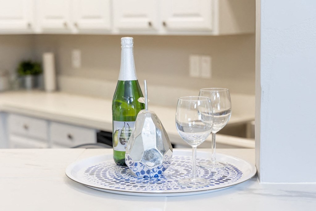 a white counter top with a plate with a bottle of wine and glasses