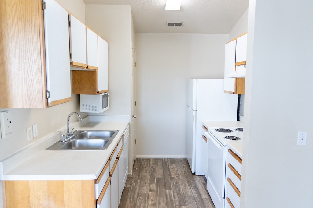 an empty kitchen with white appliances and wood flooring