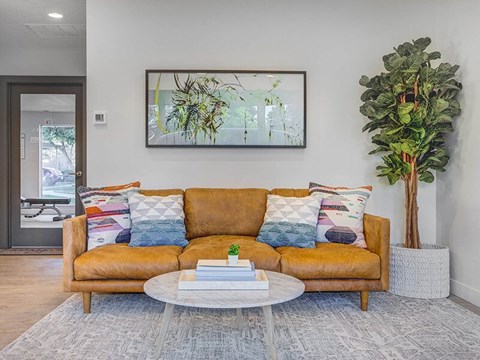 A living room with a brown couch, a white coffee table, and a painting on the wall.