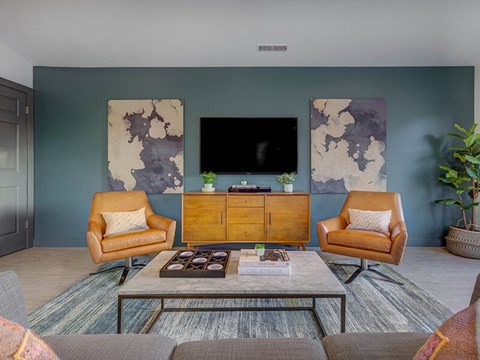 A living room with a brown chair, a brown armchair, a brown coffee table, a flat screen TV, and two paintings on the wall.