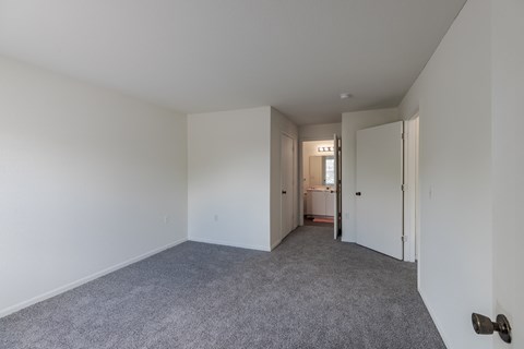 a bedroom with white walls and carpet and a door to a bathroom