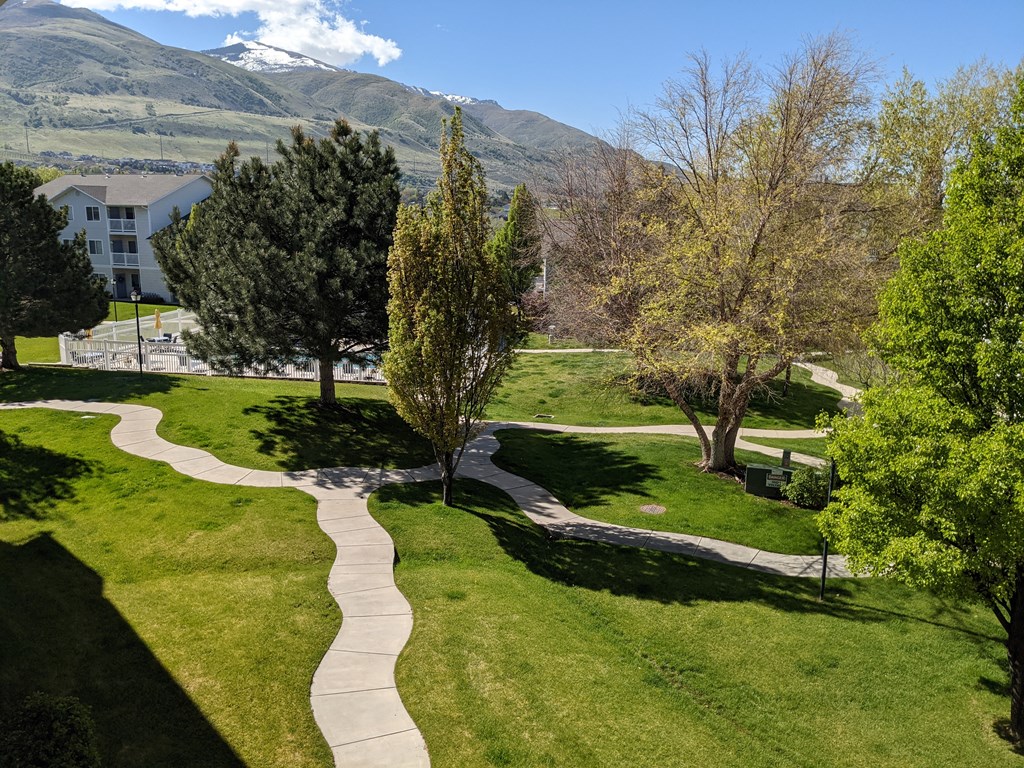a walkway through a park with trees and mountains in the background