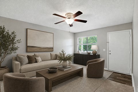 A living room with a beige couch, a brown armchair, a coffee table, and a ceiling fan.