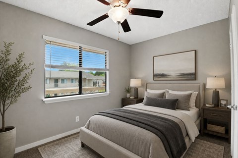 A bedroom with a large bed, a ceiling fan, and a window with blinds.