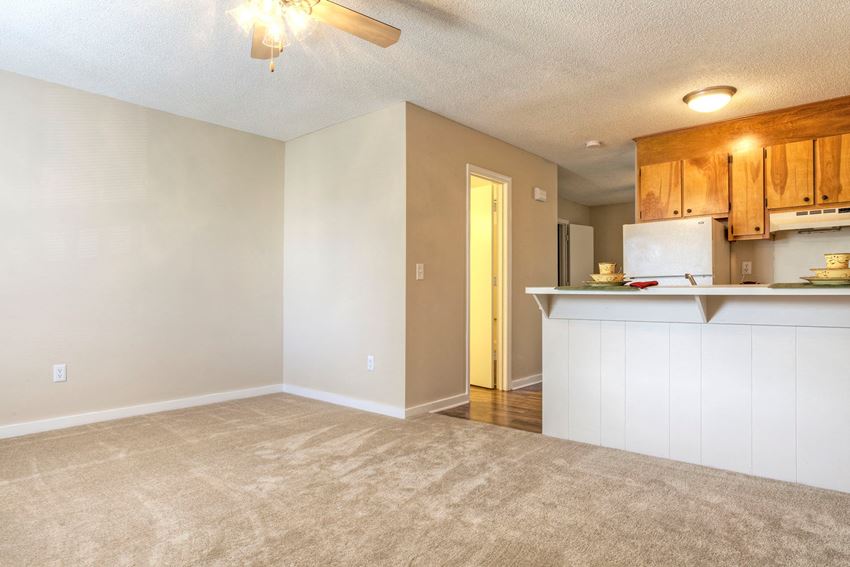 an empty living room with a kitchen in the background