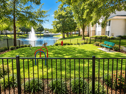 A playground with a slide and a fence in front of a pond and apartment buildings.