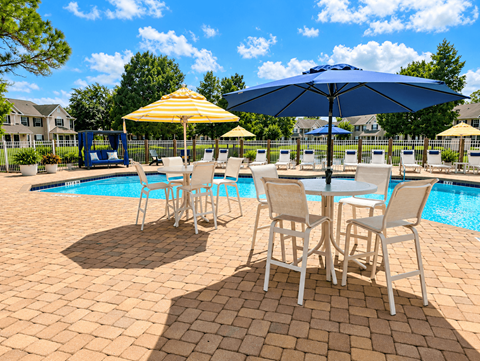 A poolside table with chairs and umbrellas is set up by a swimming pool.