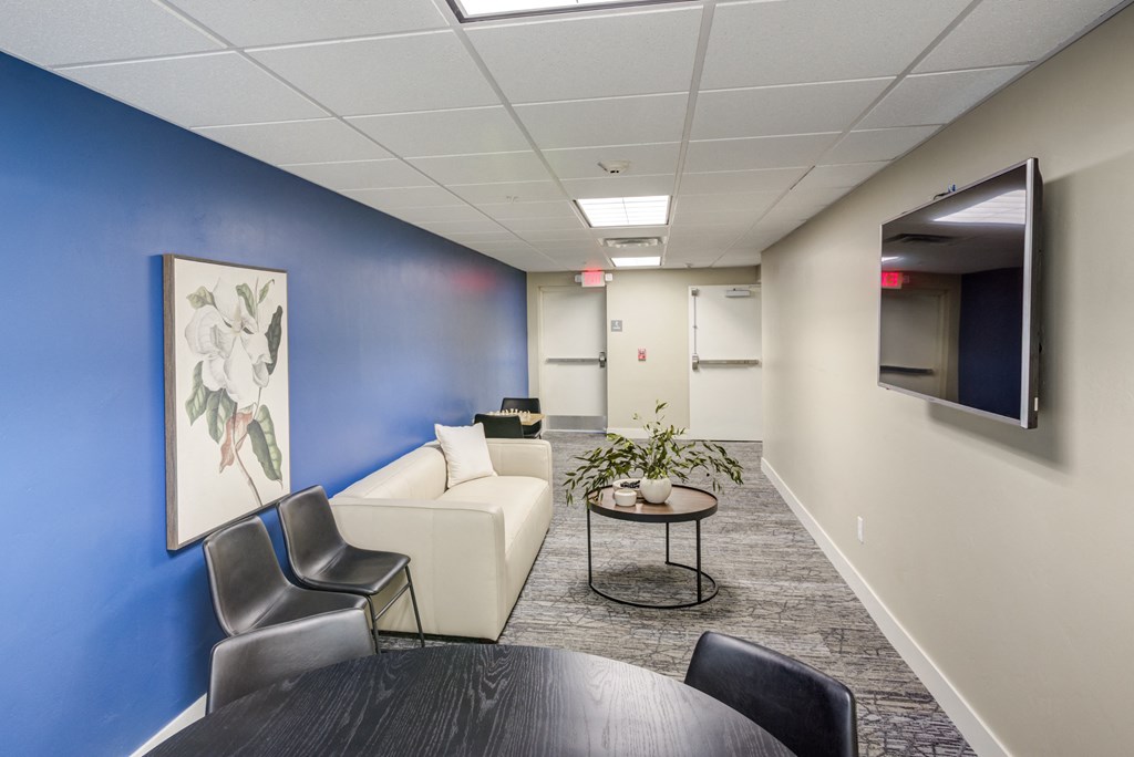 A conference room with a white couch, a coffee table, and a TV mounted on the wall.
