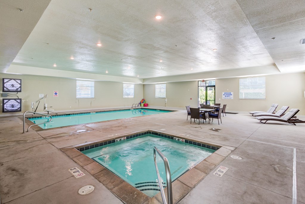 A large indoor swimming pool with a hot tub and lounge chairs.