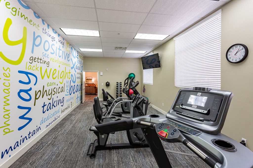 A gym room with a treadmill and a wall covered in positive words.
