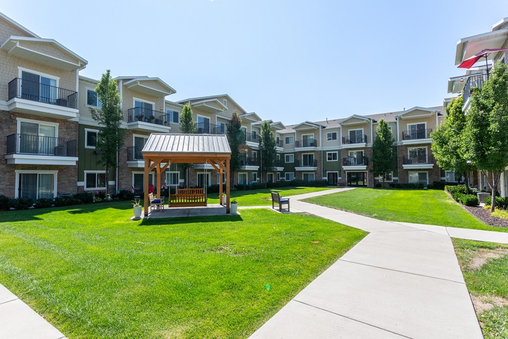 A gazebo sits in the middle of a grassy area in front of apartment buildings.