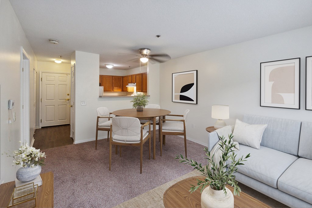 A living room with a grey couch, a wooden dining table with four chairs, and a white vase with a plant on the coffee table.