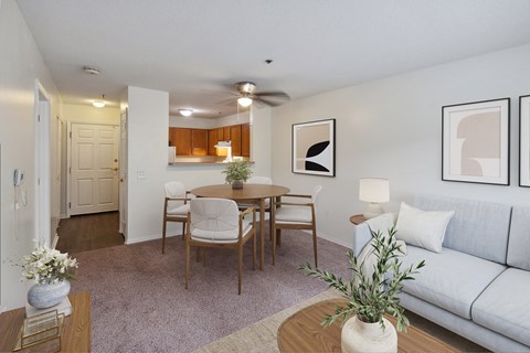 A living room with a grey couch, a wooden dining table with four chairs, and a white vase with a plant on the coffee table.
