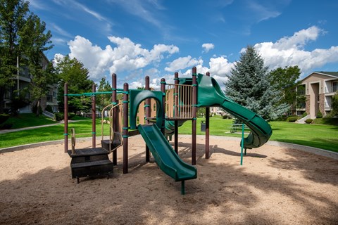A playground with a green slide and a brown sandbox.
