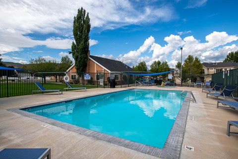 A large outdoor swimming pool surrounded by a fence and lounge chairs.