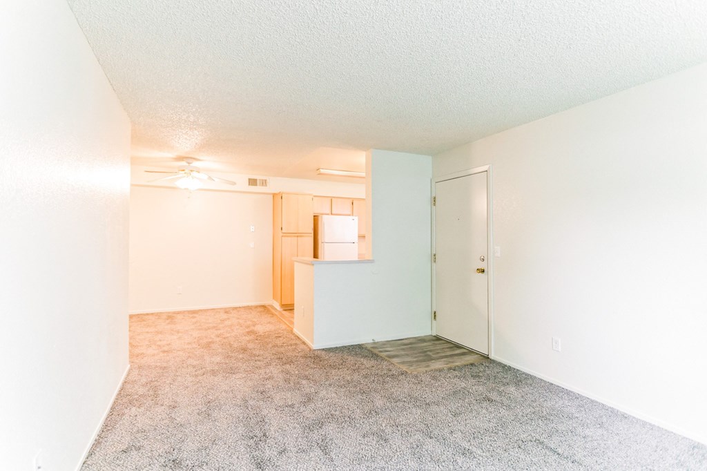 an empty living room with a kitchen in the background