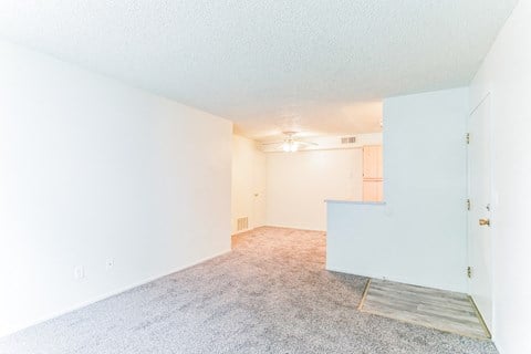 the living room and dining room of an apartment with white walls and carpet
