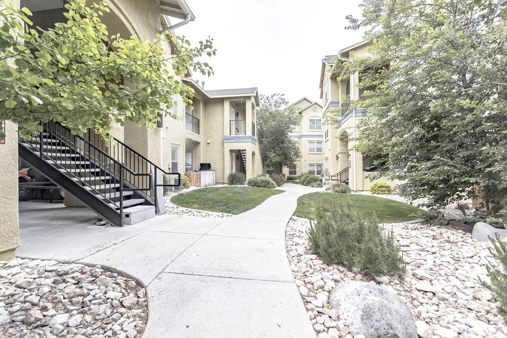 an exterior view of an apartment complex with a sidewalk and landscaping