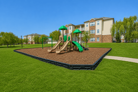 A playground with a green slide and brown sandbox in the foreground.
