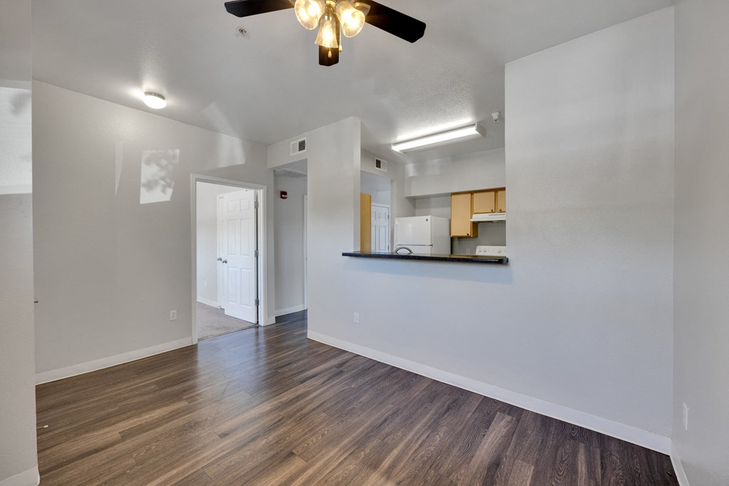 an empty living room with a ceiling fan and a kitchen