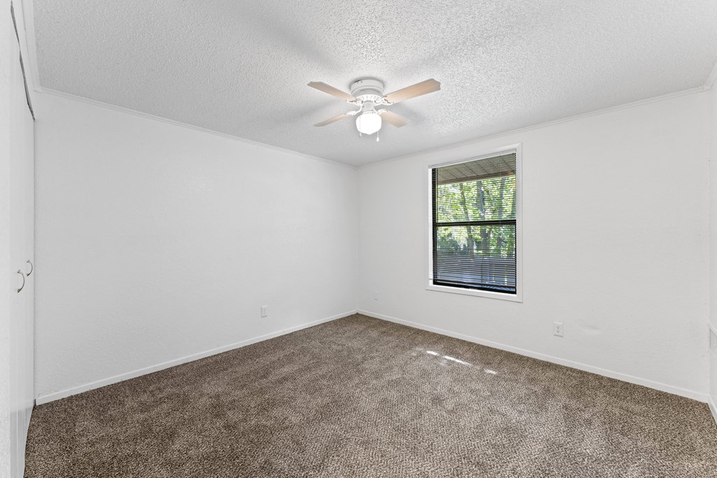 an empty living room with a ceiling fan and a window