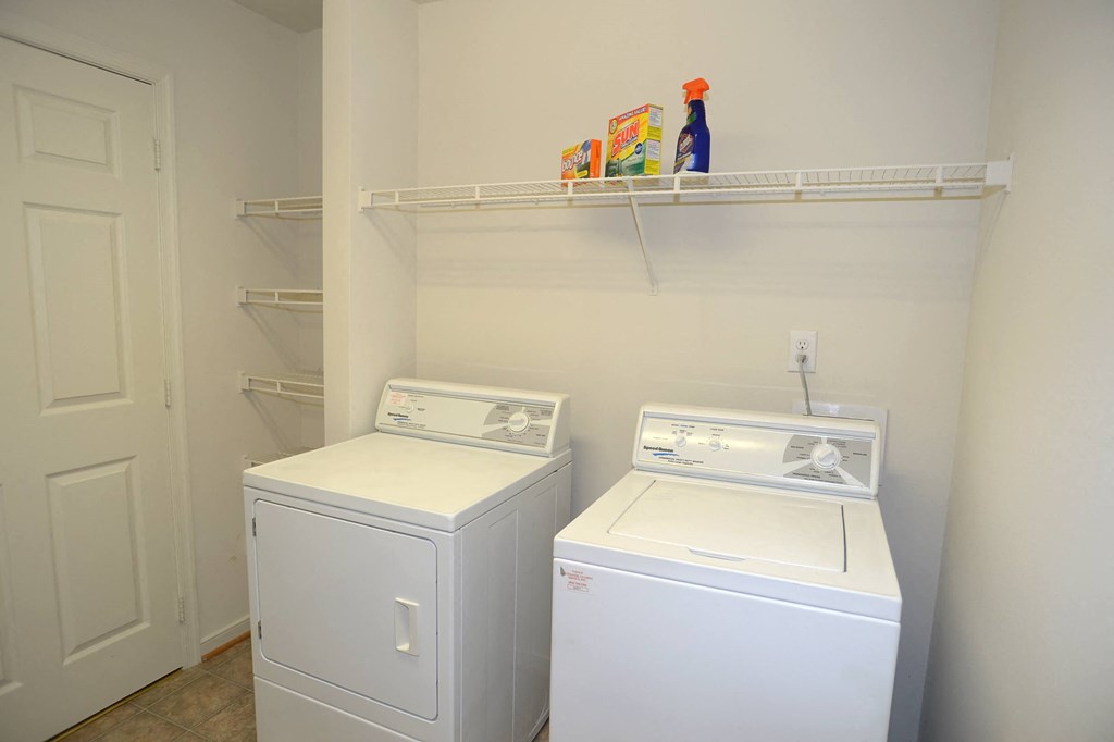 a laundry room with two washers and a dryer and a shelf above it