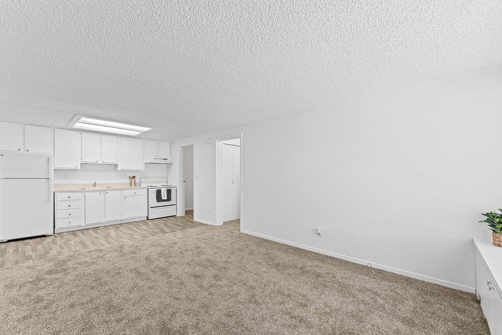 an empty living room and kitchen with white cabinets and white appliances