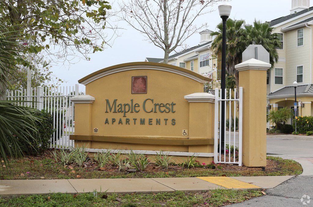 a sign for maple crest apartments in front of a fence and sidewalk