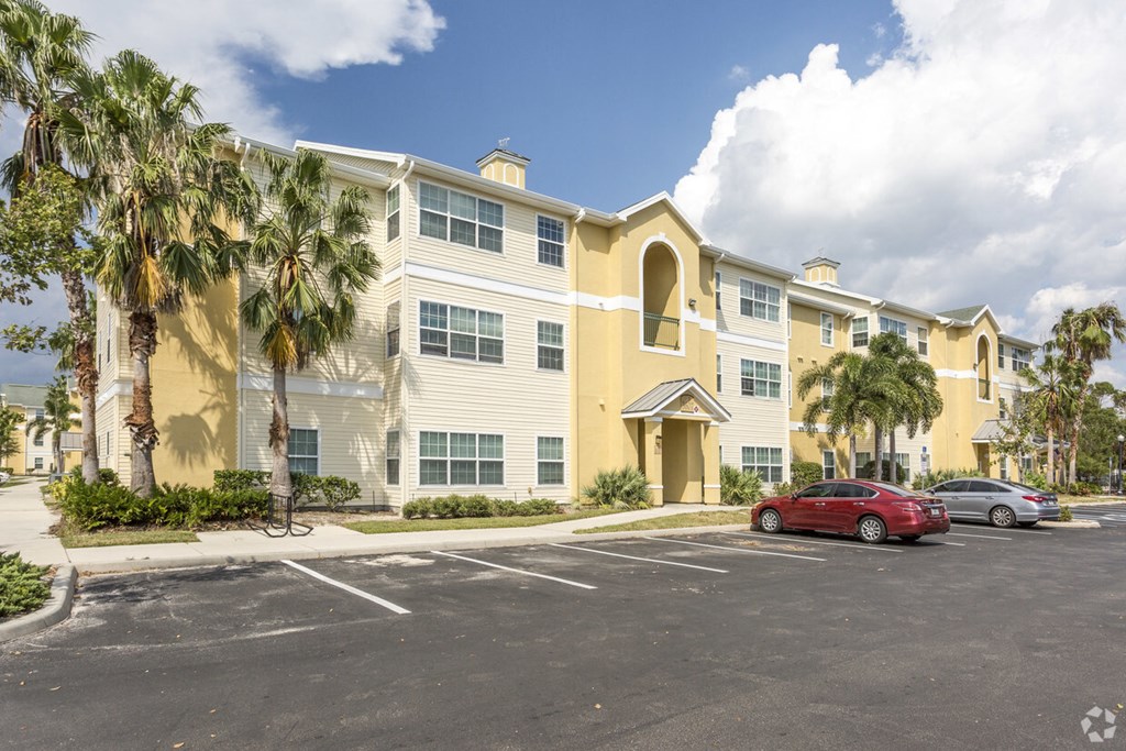 a yellow apartment building with palm trees and a parking lot