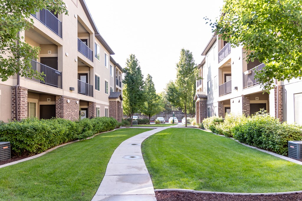 a walkway between two apartment buildings with grass and trees