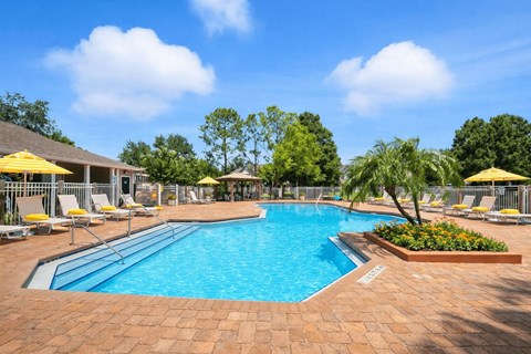 A large outdoor swimming pool surrounded by a brick patio and lounge chairs.