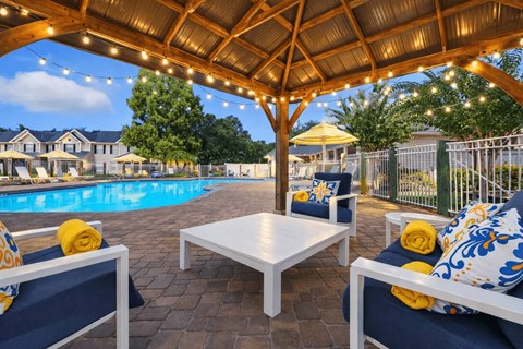 A patio with a table and chairs under a roof with lights.