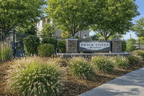 A sign that says Brick Stone in front of a fence and trees.