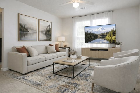 A living room with a couch, chairs, a coffee table, and a television displaying a mountain landscape.
