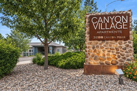 A stone sign for Canyon Village Apartments stands in front of a building.