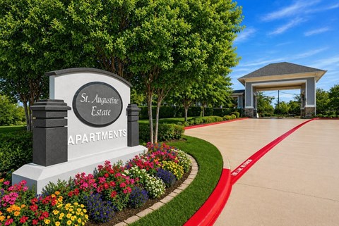 A sign for St. Augustine Estate Apartments is surrounded by flowers.