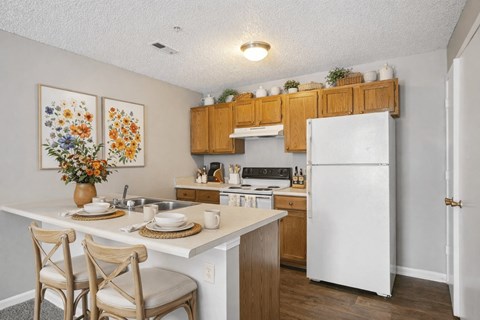 A kitchen with a white fridge, wooden cabinets, and a table with chairs.