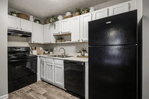 A black refrigerator stands in a kitchen with white cabinets and a black stove.