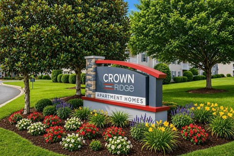 A sign for Crown Ridge Apartment Homes is surrounded by flowers.