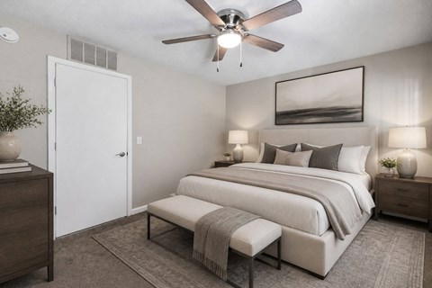 A bedroom with a large bed, a bench, and a ceiling fan.