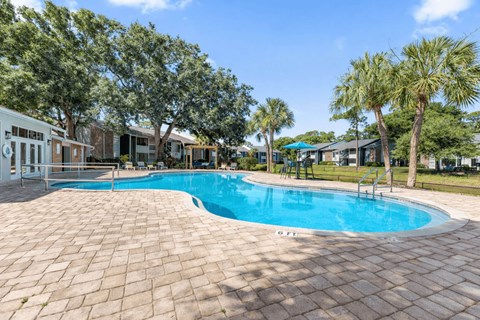 A swimming pool surrounded by a brick patio and palm trees.