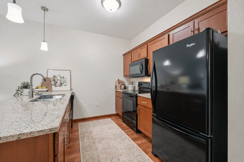 A kitchen with a black refrigerator and wooden cabinets.