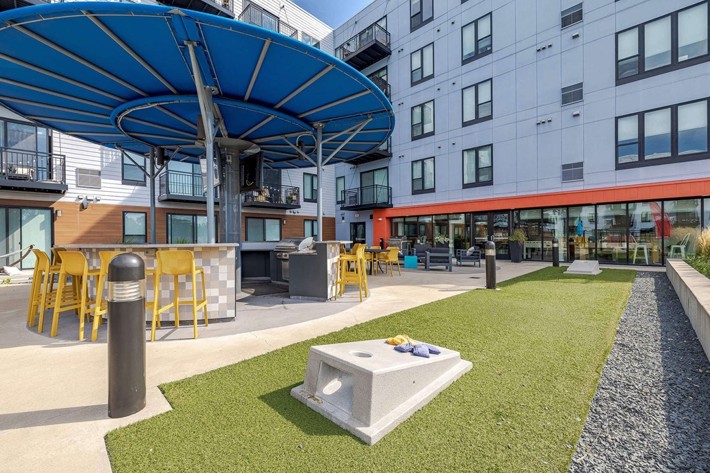 A modern outdoor seating area with a blue umbrella and yellow chairs. at Hello Apartments, Minnesota, 55427