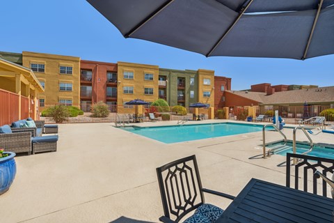 A pool area with a table and chairs and a building in the background.