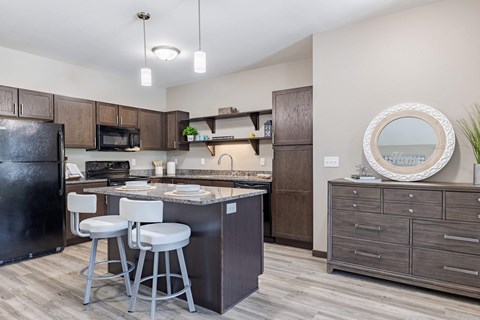 A kitchen with a black fridge, white bar stools, and a round mirror on the dresser.