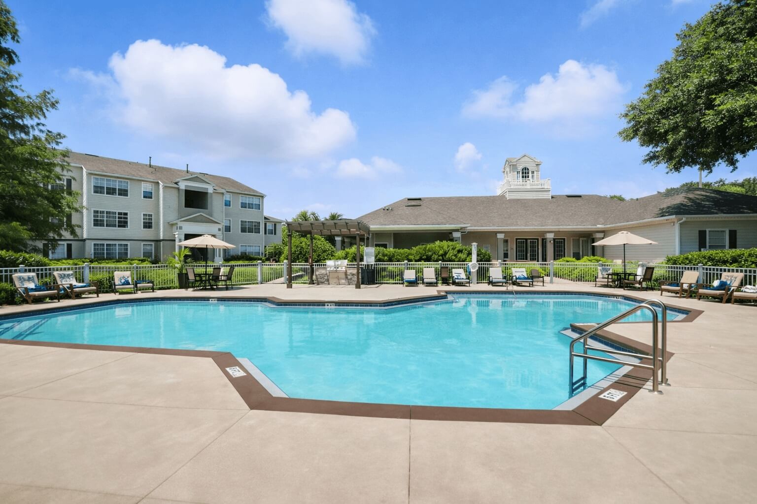 A large swimming pool surrounded by a concrete patio and a white building with a tower in the background.
