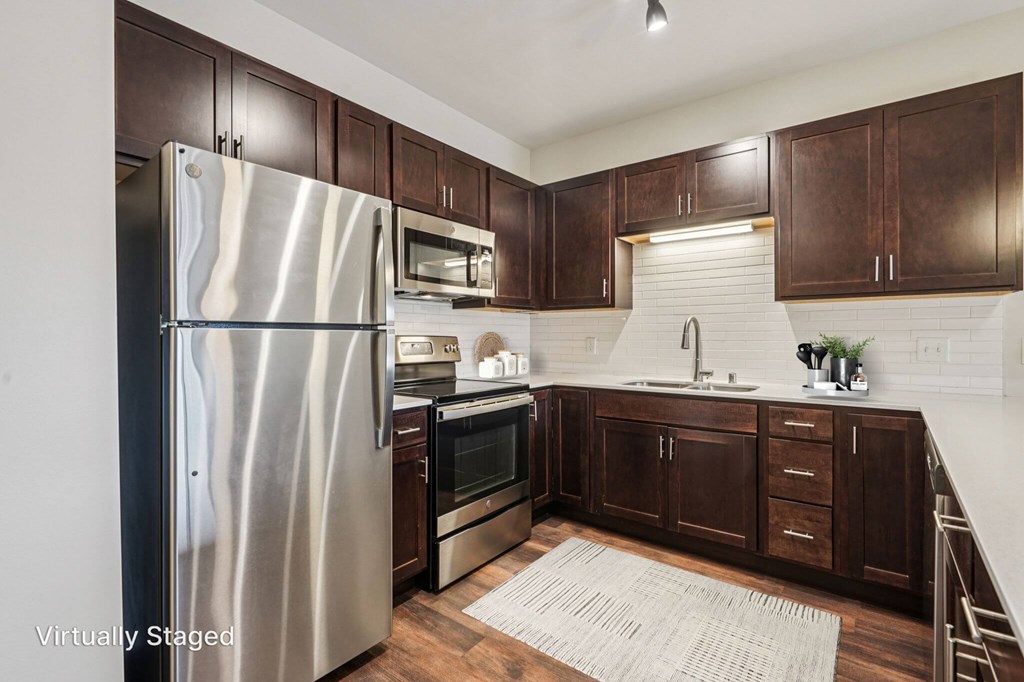 A kitchen with a stainless steel refrigerator and wooden cabinets. at Aster Meadow, Vadnais Heights, MN
