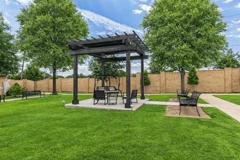 A gazebo with a table and chairs is surrounded by a grassy area.